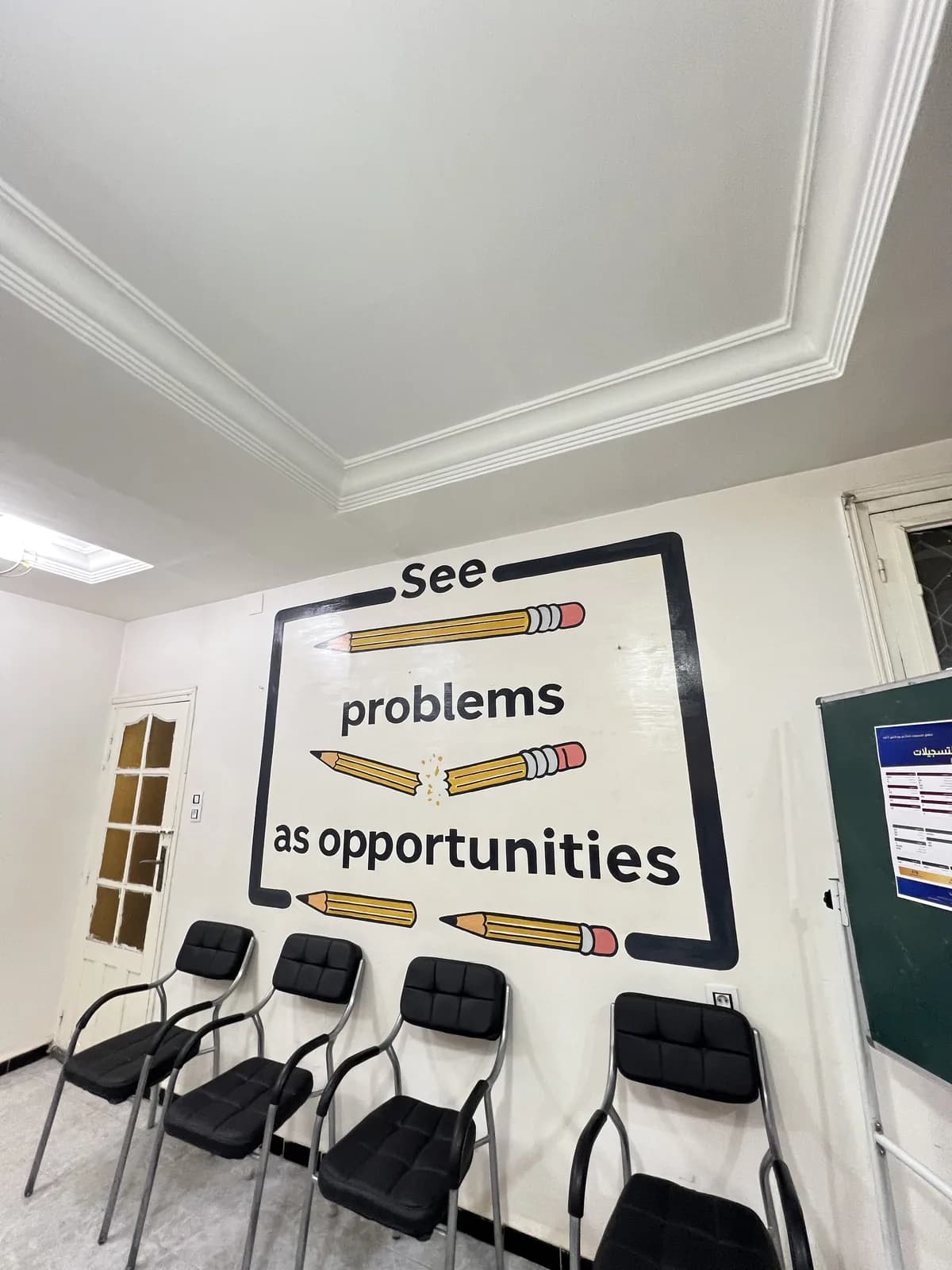قاعة دراسة بمقاعد سوداء ولوحة جدارية مكتوب عليها see problems as opportunities